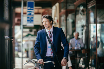 Happy middle aged businessman going to work with a bicycle in the city