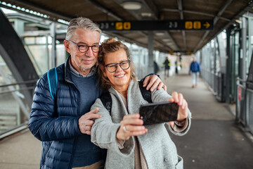 Loving elderly couple taking a selfie on smartphone at the train station