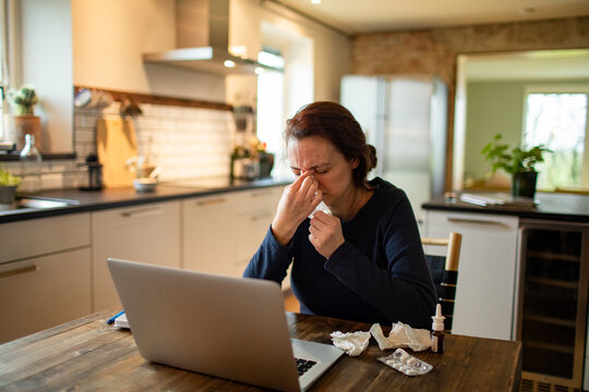 Sick woman with a cold blowing nose in a tissue at home