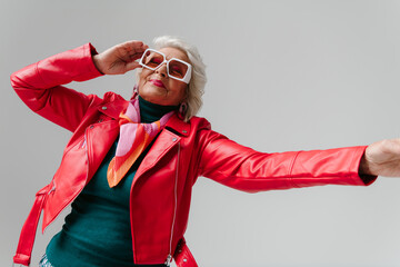 Fashionable elderly woman in leather jacket and trendy eyeglasses gesturing while dancing 
