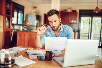 Concerned young man reading through bank statements at home