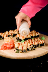 Set of sushi rolls with eel on a wooden board topped with sesame from a white bottle