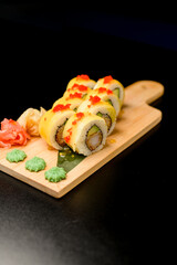 Set of sushi rolls with pieces of avocado, red caviar, ginger and wasabi on a wooden board