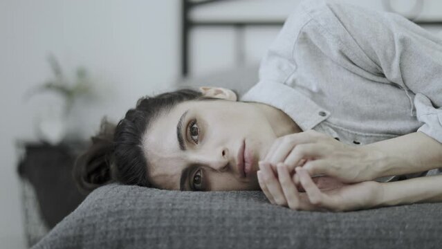 Worried woman with nervous tic touching face while lying on bed