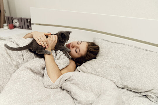 beautiful and sexy girl lying on the bed in homemade pajamas holding a happy Scottish gray kitten in her arms. purebred straight-eared British cat. blank photo frames in the form of a heart