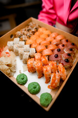 Female hands holding set of sushi rolls in a cardboard box with green wasabi and ginger