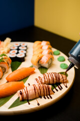 Assorted sushi rolls with sauce on a round wooden board on black table