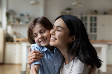 Head shot close up of happy Asian mother and Caucasian son touching cheeks, family enjoying tender moment at home together, smiling young mom hugging adorable 7s boy child, motherhood concept