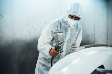 Automotive service worker in full protective gear expertly apply color paint in to car's bodywork...