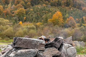 A view of the fireplace, mountains and lake. Journey to the Ukrainian Carpathians. Tongues of flame. Stones for barbecue. Warming up by the fire. Romance of the mountains. Fall nature.