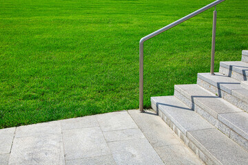 granite sidewalk with stone stairs and steel railings along a green lawn on a sunny summer day, a landscaped park for walking, nobody.