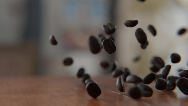 Coffee beans falling on and bouncing off of the wooden table