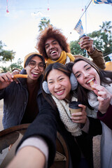 Vertical selfie phone looking camera of cheerful friends eating chocolate churros street food stall outdoors. Generation z tourist group of happy people having fun in terrace cafeteria in winter time