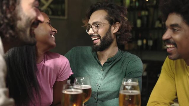 Young group of happy people drinking cold beer at brewery pub. Multiracial colleagues enjoying happy hours after work toasting beer at bar