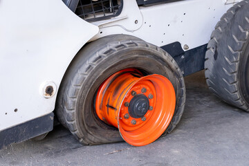 Close-up view of a flat or torn tire on a compact forklift or compact loader. A broken car is waiting for repair in a car repair shop. Malfunction of municipal equipment