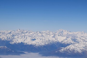 Beautiful aerial view of alpine snowcapped mountain range peaking through heavy clouds. Mountain...