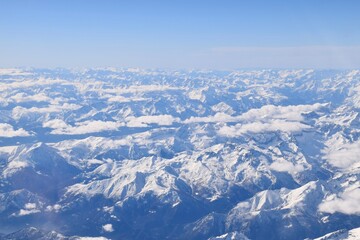 Fototapeta na wymiar Beautiful aerial view of alpine snowcapped mountain range peaking through heavy clouds. Mountain peaks of Italian alps from above. The impressive winter view is taken from an airplane window.
