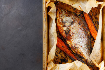 Baked dorado fish with golden crust and carrot on baking tray. Top view. Copy space