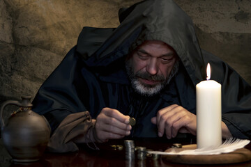 Portrait of a monk in a cassock, counting money by candlelight in a dark stone room, stacks of coins. In the Middle Ages - tax collector, church treasurer. - obrazy, fototapety, plakaty