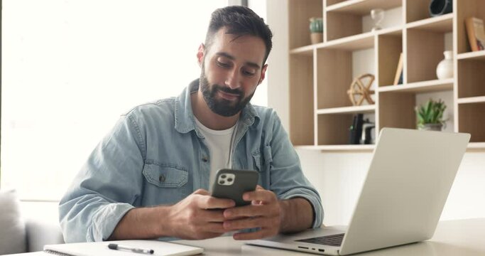 Handsome Hispanic businessman using cellphone sit at workplace, share text messages by business, lead personal chat, distracted from work spend time on internet, enjoy new e-dating apps for singles