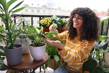 Beautiful young woman spraying potted houseplants with water on balcony