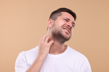 Allergy symptom. Man scratching his neck on light brown background