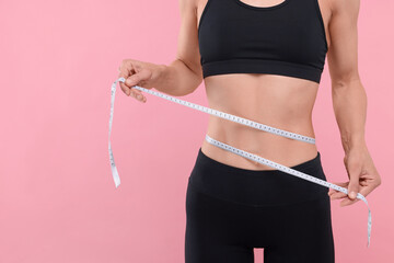 Slim woman measuring waist with tape on pink background, closeup and space for text. Weight loss