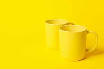 Two ceramic mugs on yellow background, space for text