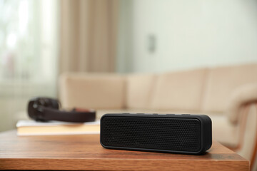 One black portable bluetooth speaker on wooden table indoors, space for text. Audio equipment