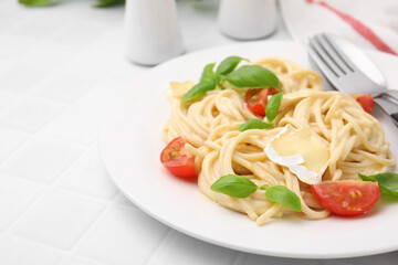 Delicious pasta with brie cheese, tomatoes, basil and cutlery on white tiled table, closeup. Space for text
