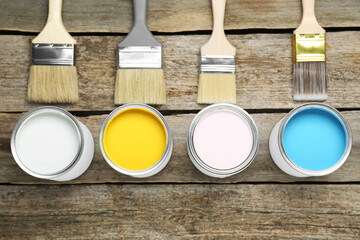 Cans of colorful paints with brushes on wooden table, flat lay