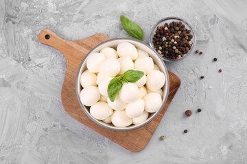 Tasty mozzarella balls and basil leaves in bowl on grey table, flat lay
