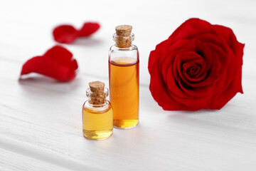 Bottles of essential oil and red rose flower on white wooden table
