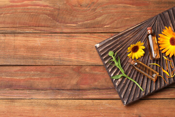 Bottles of essential oils and beautiful calendula flowers on wooden table, top view. Space for text