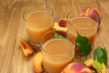 Glasses of peach juice, fresh fruits and leaves on wooden table