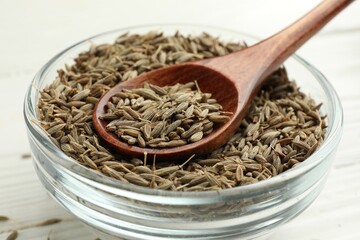Bowl of caraway seeds and spoon on white table, closeup