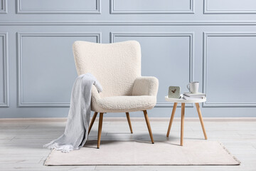 Comfortable armchair with blanket and side table indoors - obrazy, fototapety, plakaty