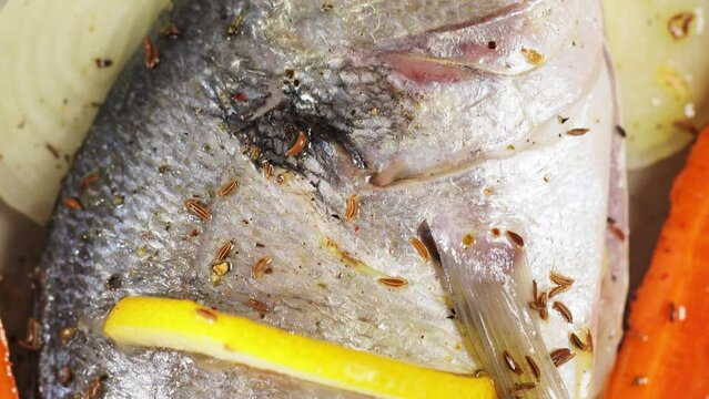 Fresh uncooked fish dorado with lemon, cumin seeds and carrot on parchment paper. Top view