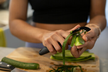 A woman peels cucumber, which protects nerve cells, improves memory and prevents Alzheimer's disease - obrazy, fototapety, plakaty
