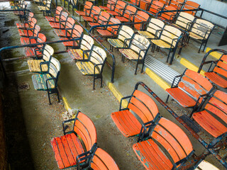 Old faded orange and yellow painted wooden seats at a abandoned a stadium grandstand.
