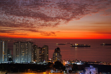 Fototapeta na wymiar Atardecer en la costa de la ciudad, con el mar y sus olas, el sol se ve naranja en el horizonte