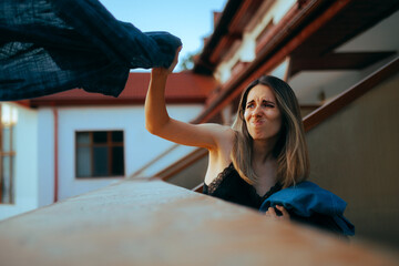 Furious Girlfriend Throwing Boyfriend Clothes Over the Balcony. Angry woman feeling vindictive after her husband betrayed her 
