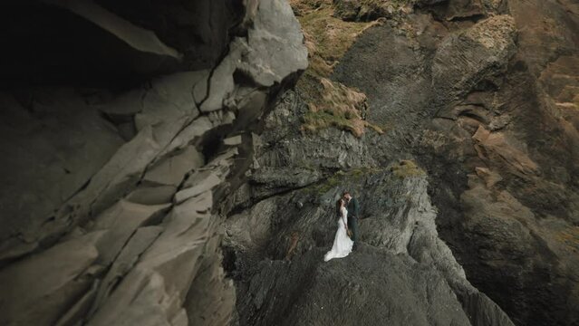 The tiny figures of a young bride and groom in the majesty of the bleak cliffs of wilderness of south coast of Iceland. Extreme and memorable wedding venue. High quality 4k footage