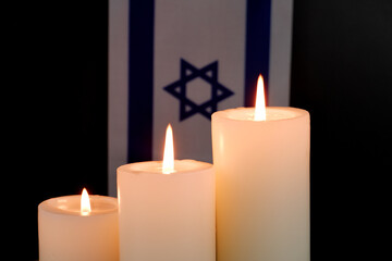 Flag of Israel and three different white burning candles on black background. Memorial and pray...