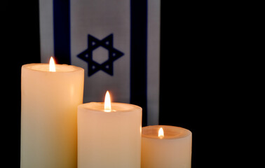 Flag of Israel and three different white burning candles on black background. 