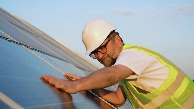 Close up of an senior engineer hand is checking an operation of sun and cleanliness of photovoltaic solar panels on a sunset