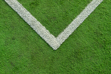 the line of the corner quadrant of a synthetic grass soccer field that is a little worn and soiled