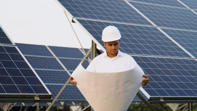 Indian engineer in protective helmet checks technical documentation of the solar station after installation