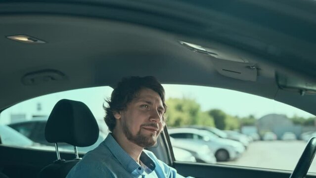 An attractive long-haired man in his budget and practical car. A satisfied and calm driver sits and enjoys life, because everything is fine with him.