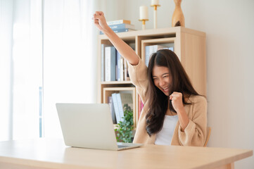 Happy euphoric young asian woman celebrating winning or getting ecommerce shopping offer on computer laptop. Excited happy girl winner looking at notebook celebrating success